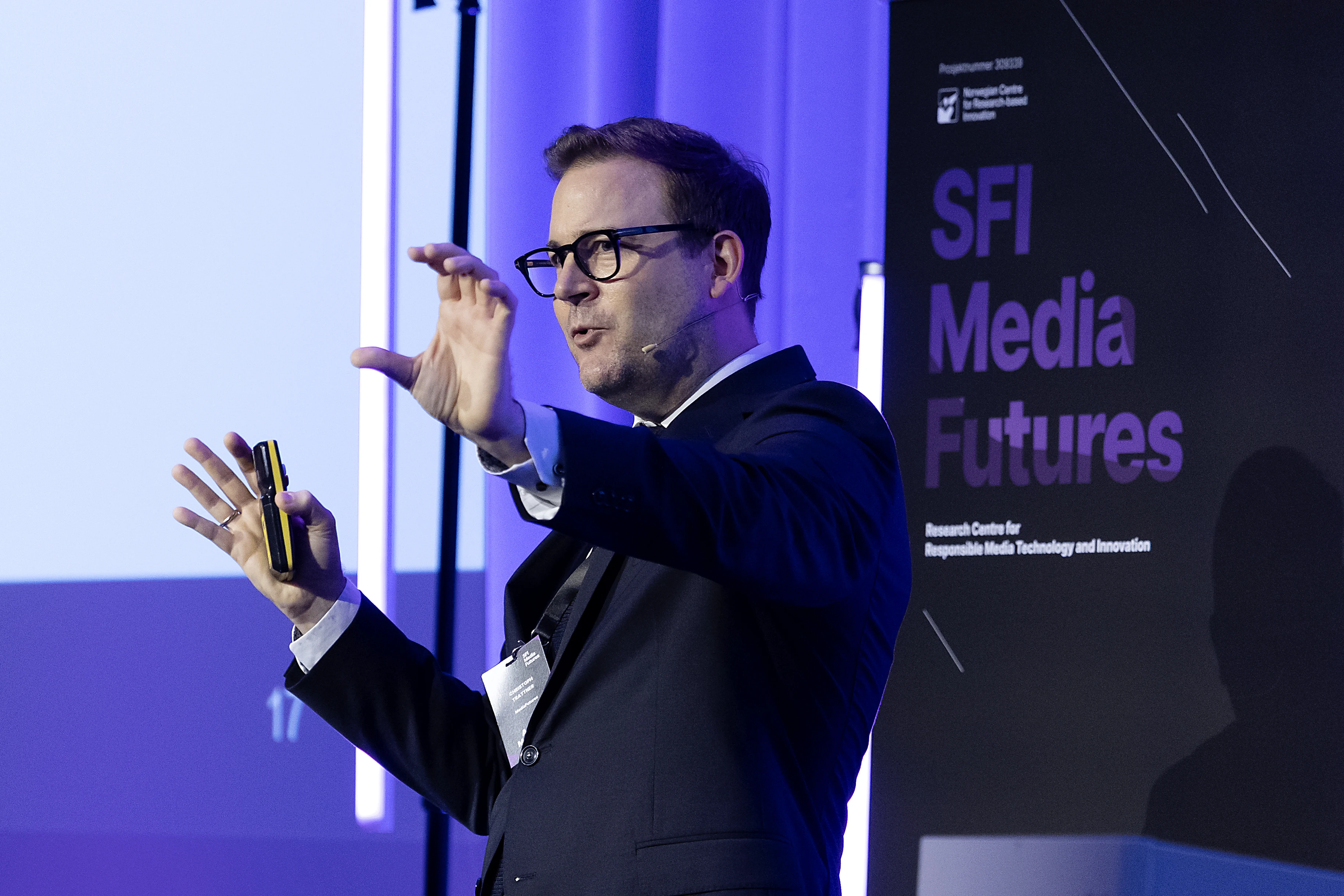 Christoph Trattner speaking with expressive hand movements in front of the SFI MediaFutures banner.